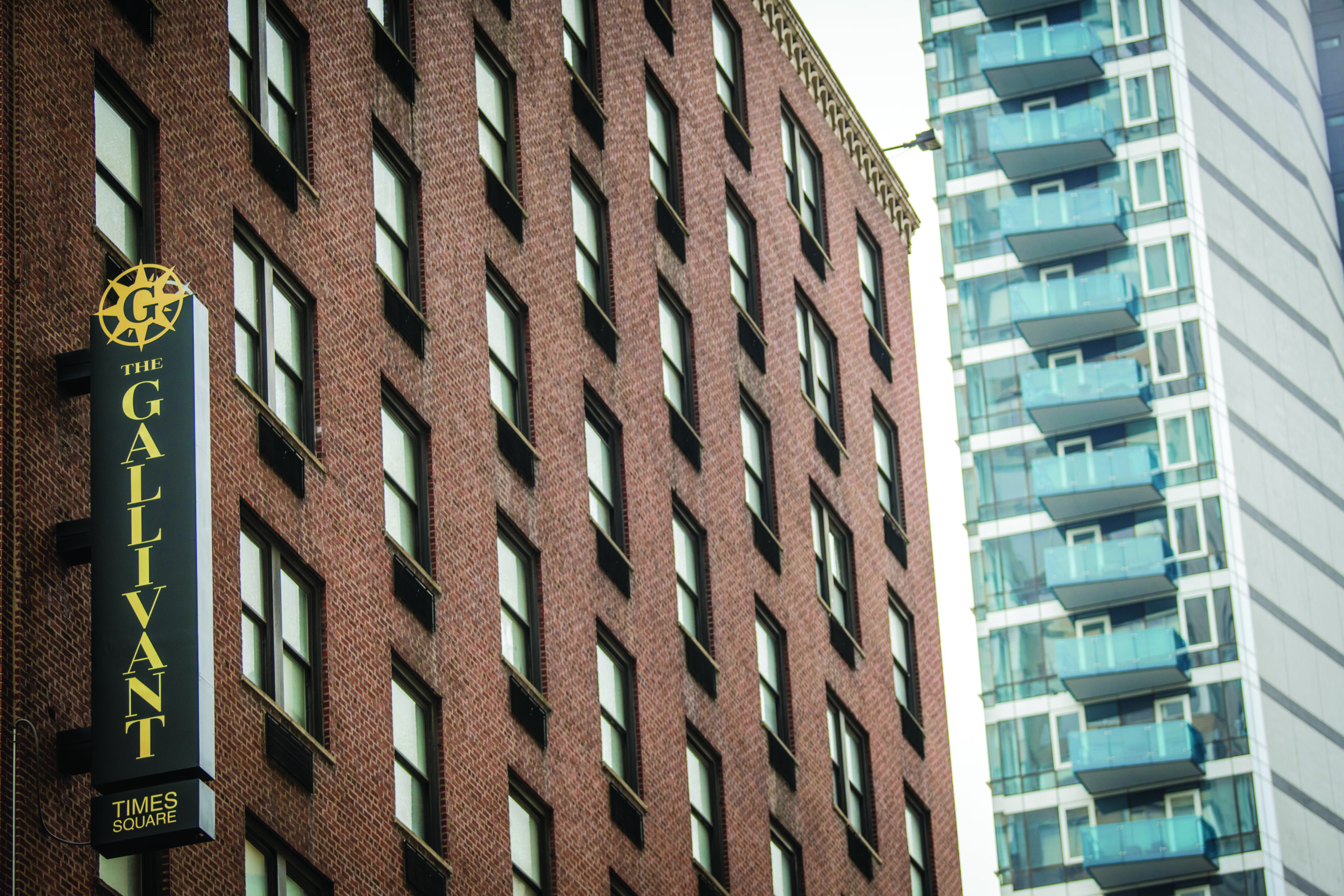 Sign for The Gallivant Times Square, a Braintrust hotel, displayed on a brick building next to a modern glass high-rise.