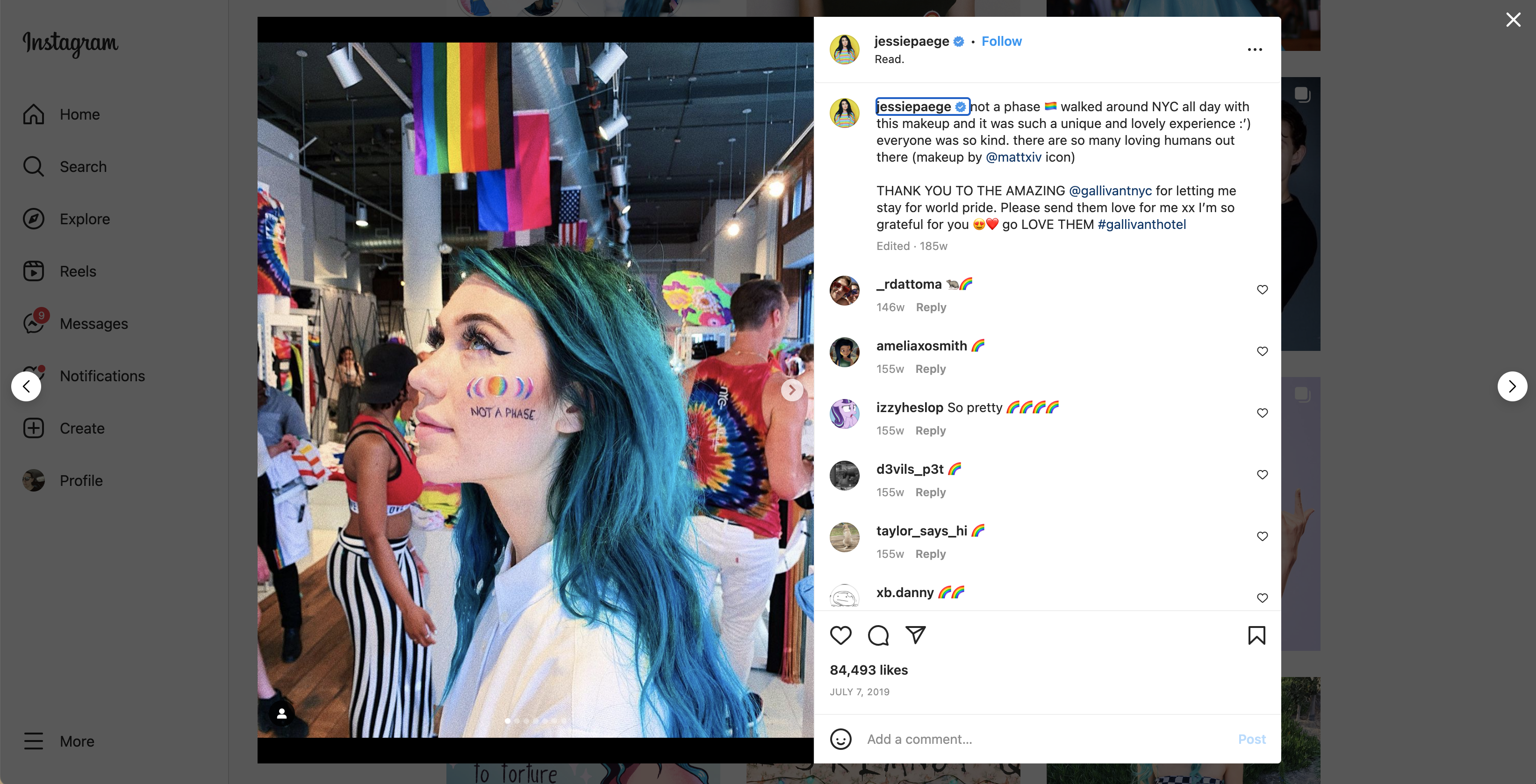 Woman with blue hair and rainbow face paint stands in a shop decorated with pride flags and people in colorful outfits.
