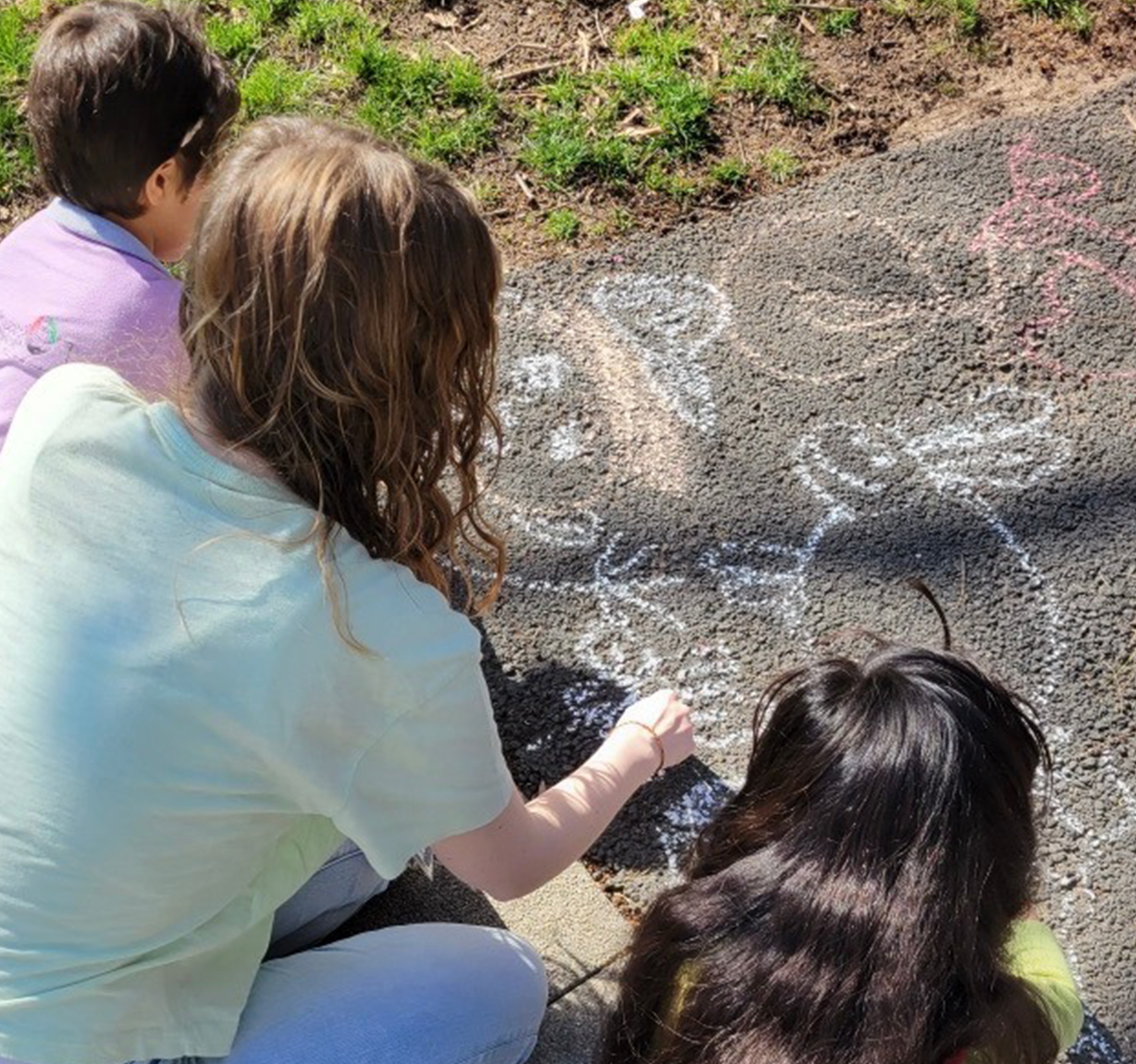 Three children from Braintrust create colorful chalk art on a paved surface outside the National Conference Center on a sunny day.