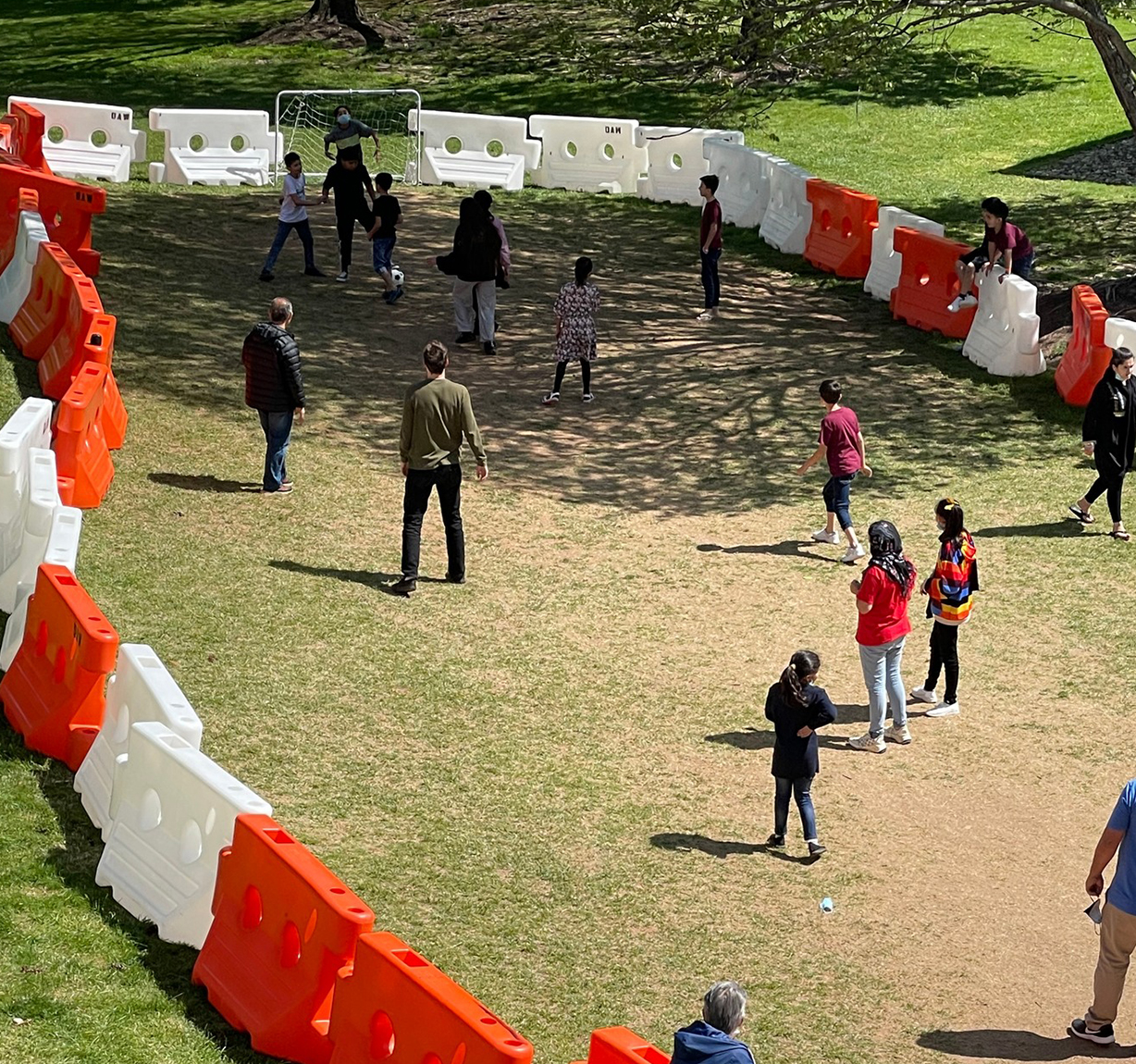 Children and adults play soccer inside a circular area surrounded by orange and white barriers on grass at the Braintrust event held at the National Conference Center.