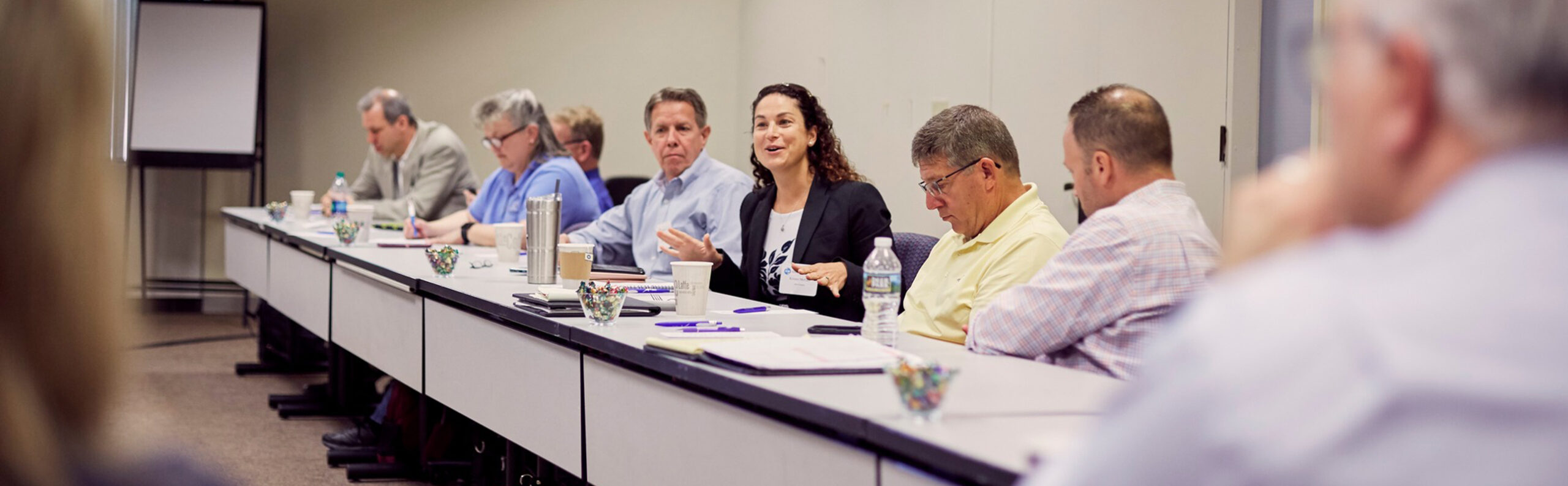 At the National Conference Center, a braintrust gathers around a conference table, with one woman speaking as others listen and take notes.