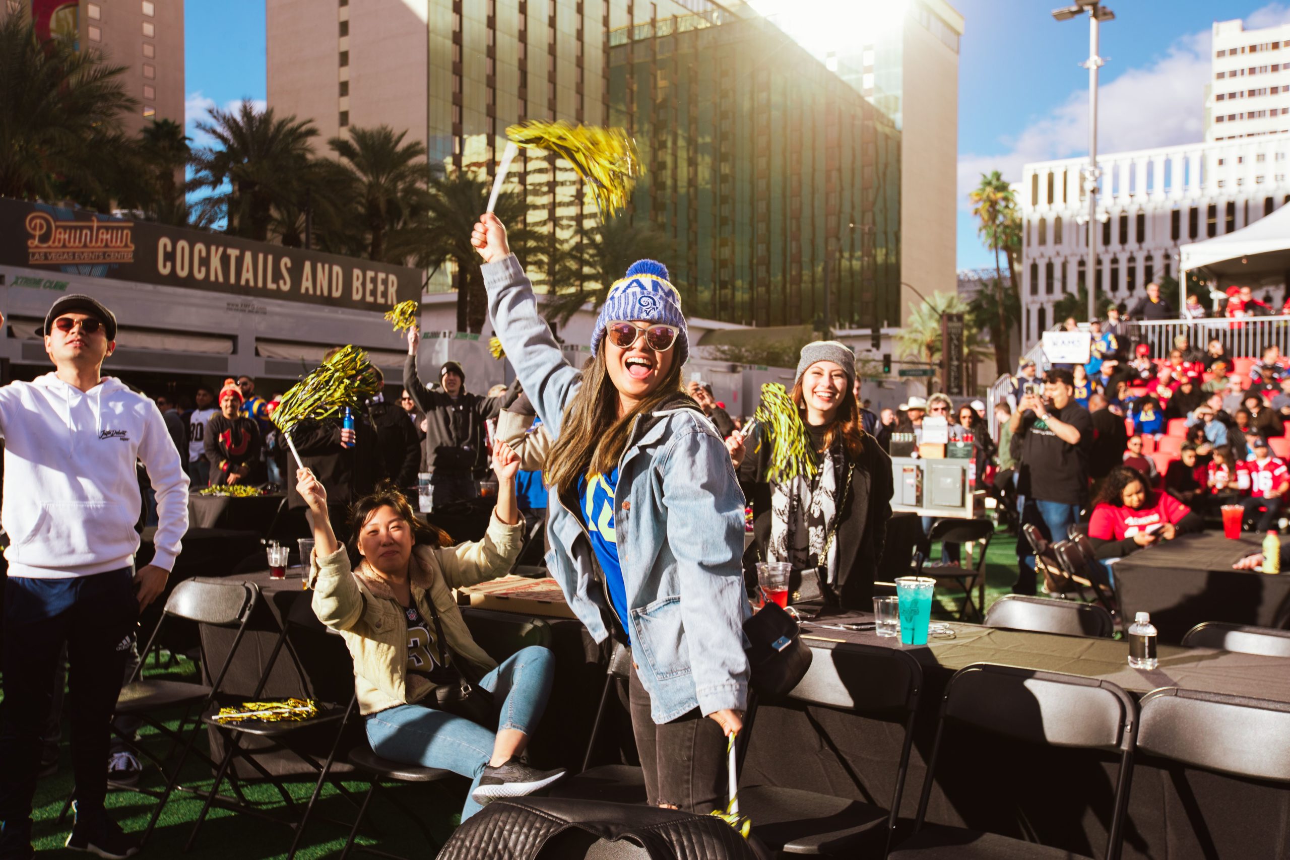 Fans in outdoor seating at DLVEC cheer enthusiastically at a sports event, waving yellow pom-poms under sunny skies—a true Braintrust of excitement.
