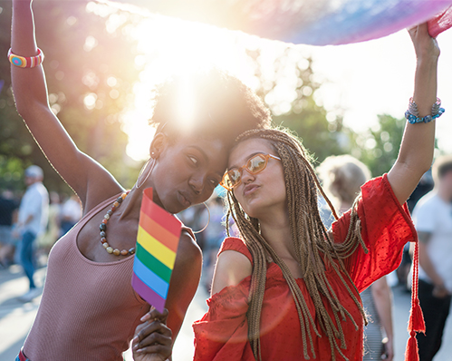 Two people smiling and holding a rainbow pride flag at an outdoor Braintrust event, sunlight shining behind them as they gallivant through Times Square.