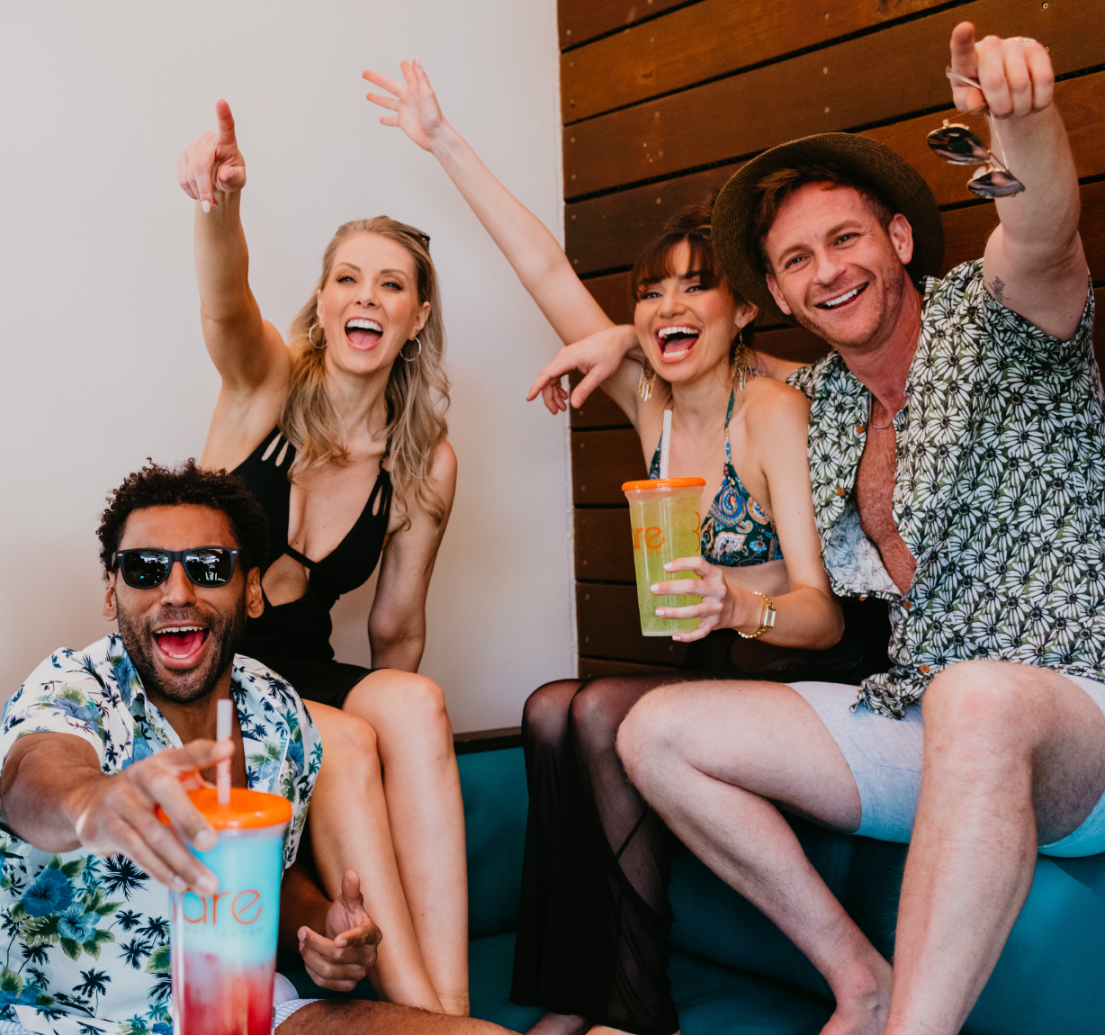 Four friends sit on a couch at the National Conference Center, smiling, holding drinks, and pointing excitedly toward the camera—capturing the spirit of connection at this year’s Braintrust event.