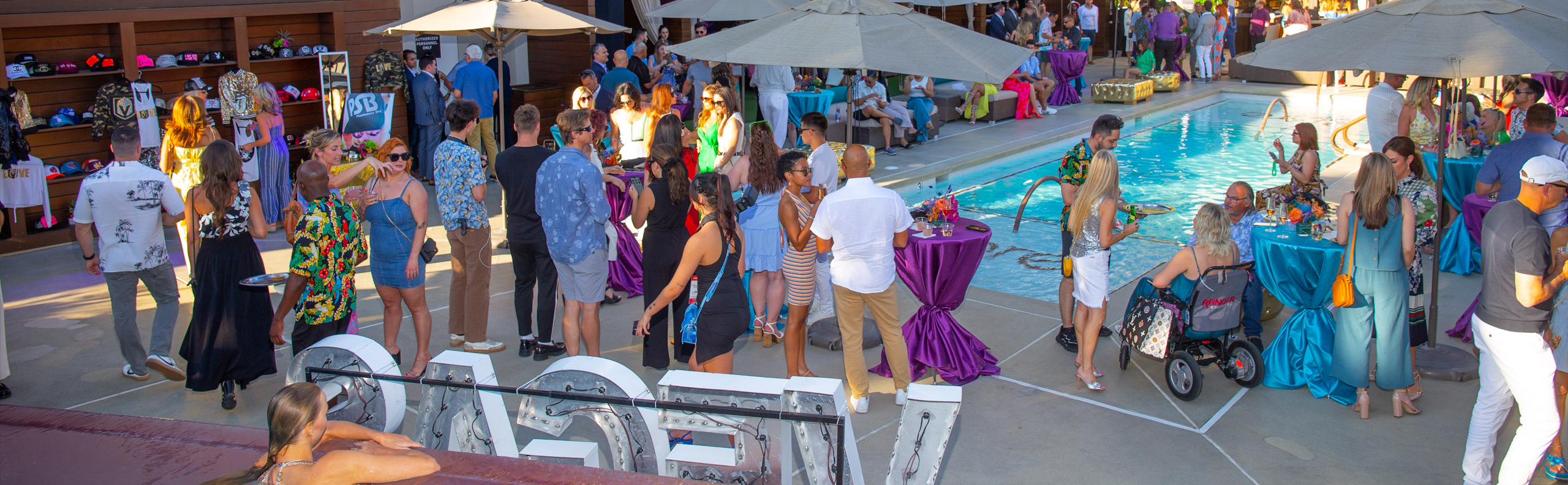 People gather around a pool at an outdoor event at the National Conference Center, featuring tables, umbrellas, large decorative letters, and lively Braintrust discussions.