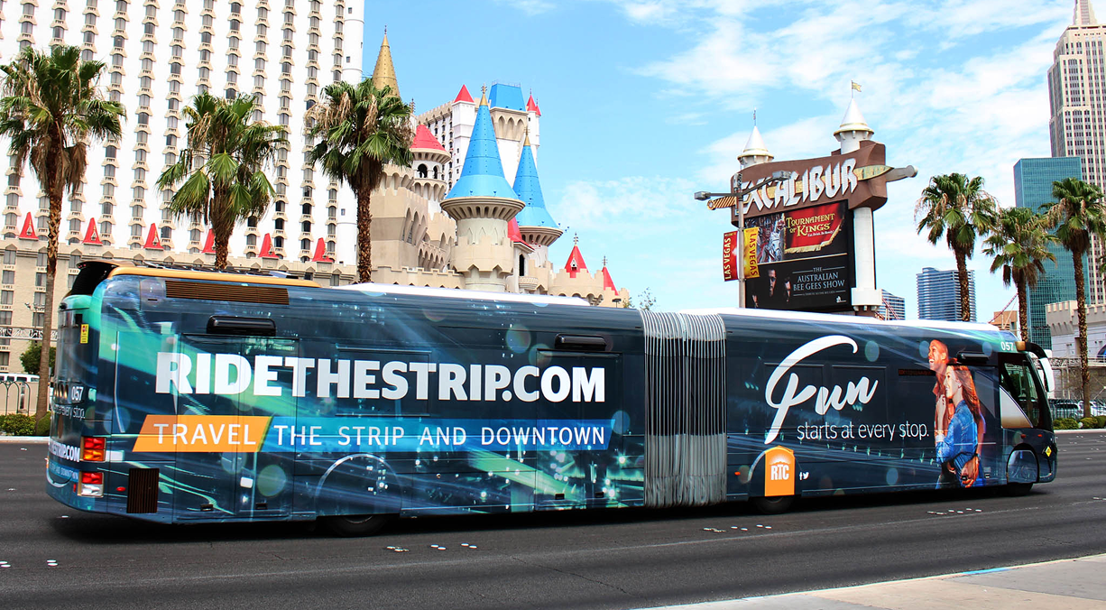 A city bus with RIDETHESTRIP.COM advertising travels past palm trees and casinos on the Las Vegas Strip.
