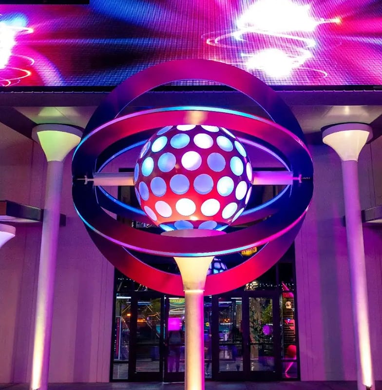 A glowing, futuristic orb sculpture with purple and blue lights outside a building at night.
