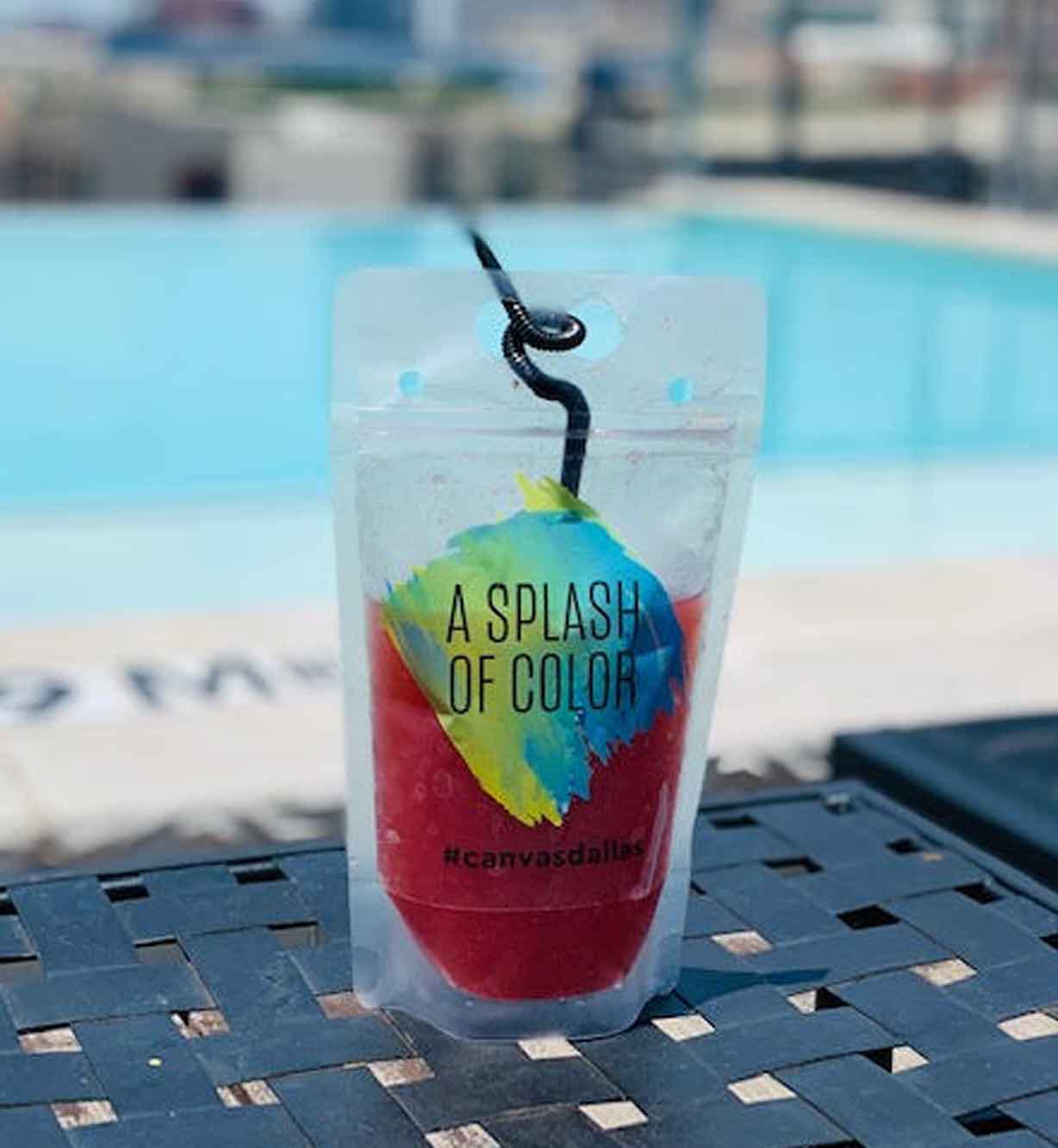 A red frozen drink in a pouch with a straw, labeled A Splash of Color, by a poolside.