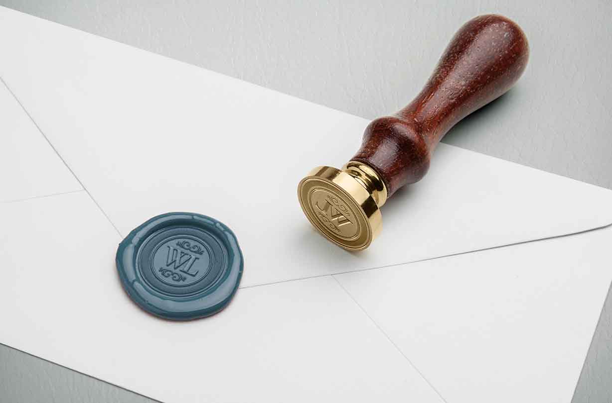 A sealed white envelope with a blue wax seal and a wooden-handled brass stamp next to it.