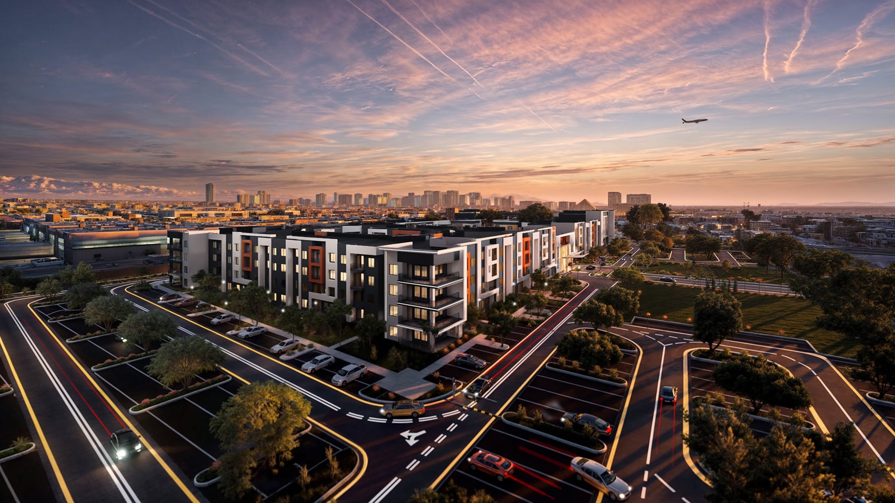 Modern apartment complex at sunset with city skyline, airplane in sky, and cars in parking lot and streets.
